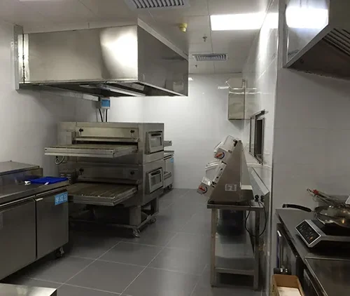 Conveyor pizza oven in a commercial kitchen installation with prep table and dough equipment
