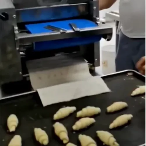 Croissant moulder production scene dough rolls onto baking tray